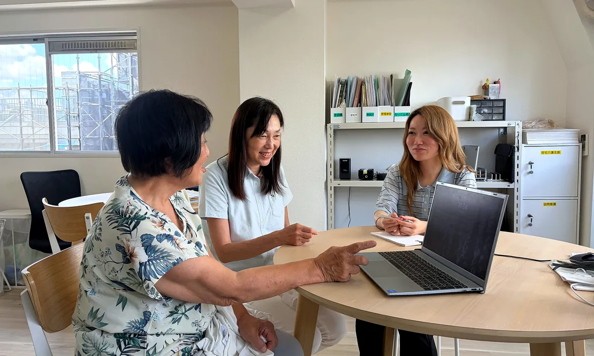 事務所の丸テーブルでノートパソコンを見ながら打ち合わせをする3人のケアマネジャー