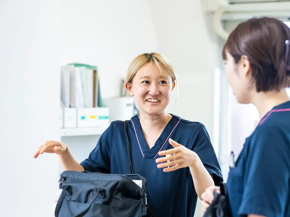訪問用バッグを肩にかけ、同僚と笑顔で話す訪問看護スタッフ