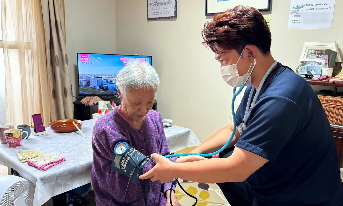 利用者さまのご自宅の居間で血圧を測る看護師