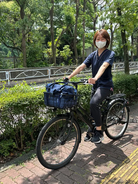 訪問用バッグを前かごに入れ、電動自転車で訪問に向かうスタッフ